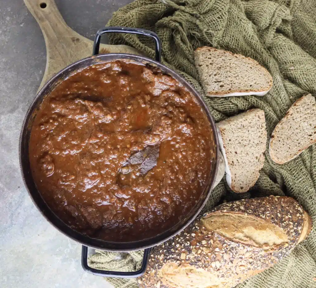 A huge pot of cooked gulasz wolowi (polish beef goulash) with fresh bread in the background