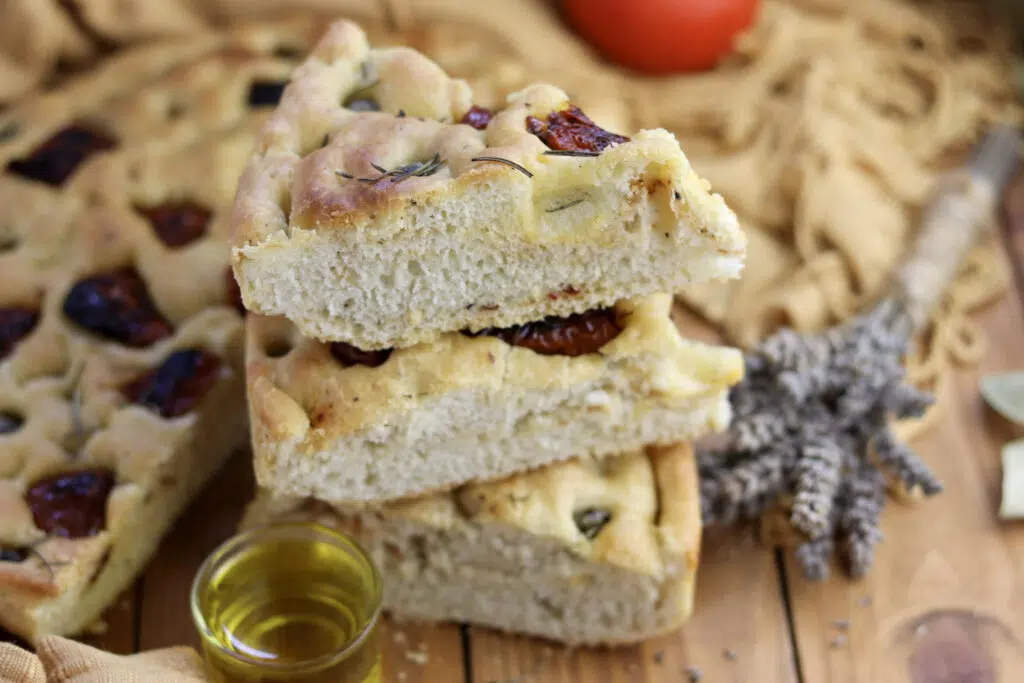 three pieces on top of eachother with the rest of the focaccia with sun dried tomatoes in the background