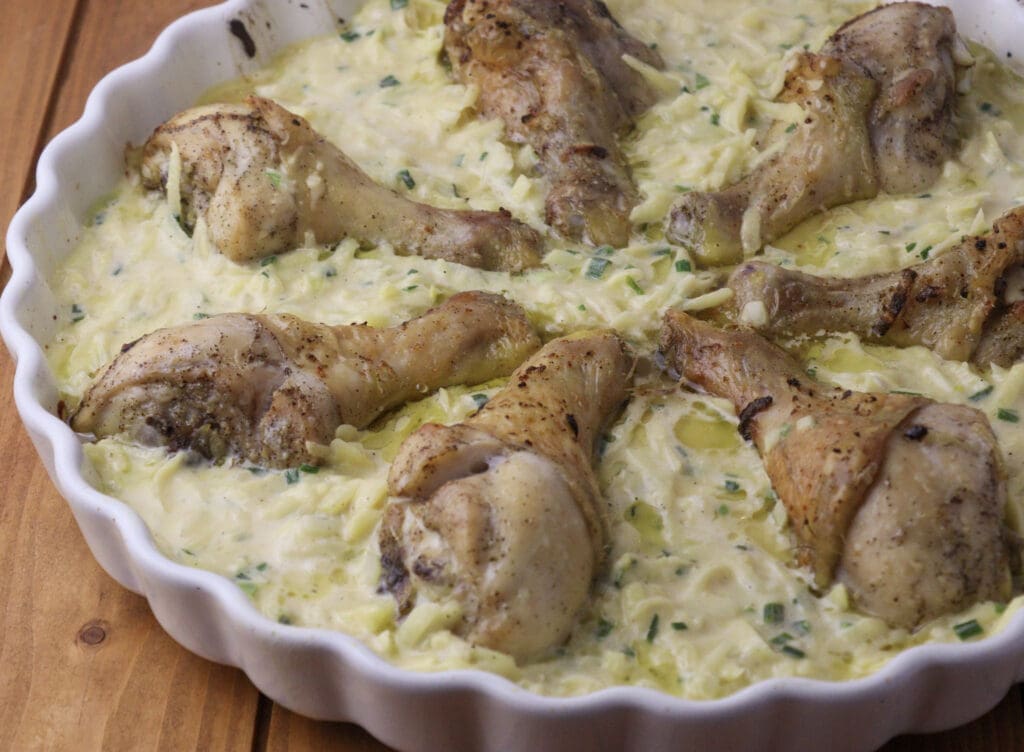 Image showing how to add the potato batter to the pan together with half baked chicken drumsticks