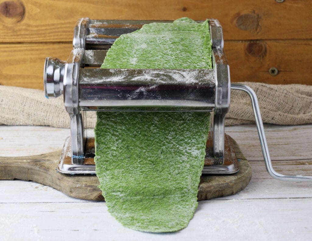 rolling a first sheet of green wild garlic pasta dough on the first setting of the pasta maker machine 