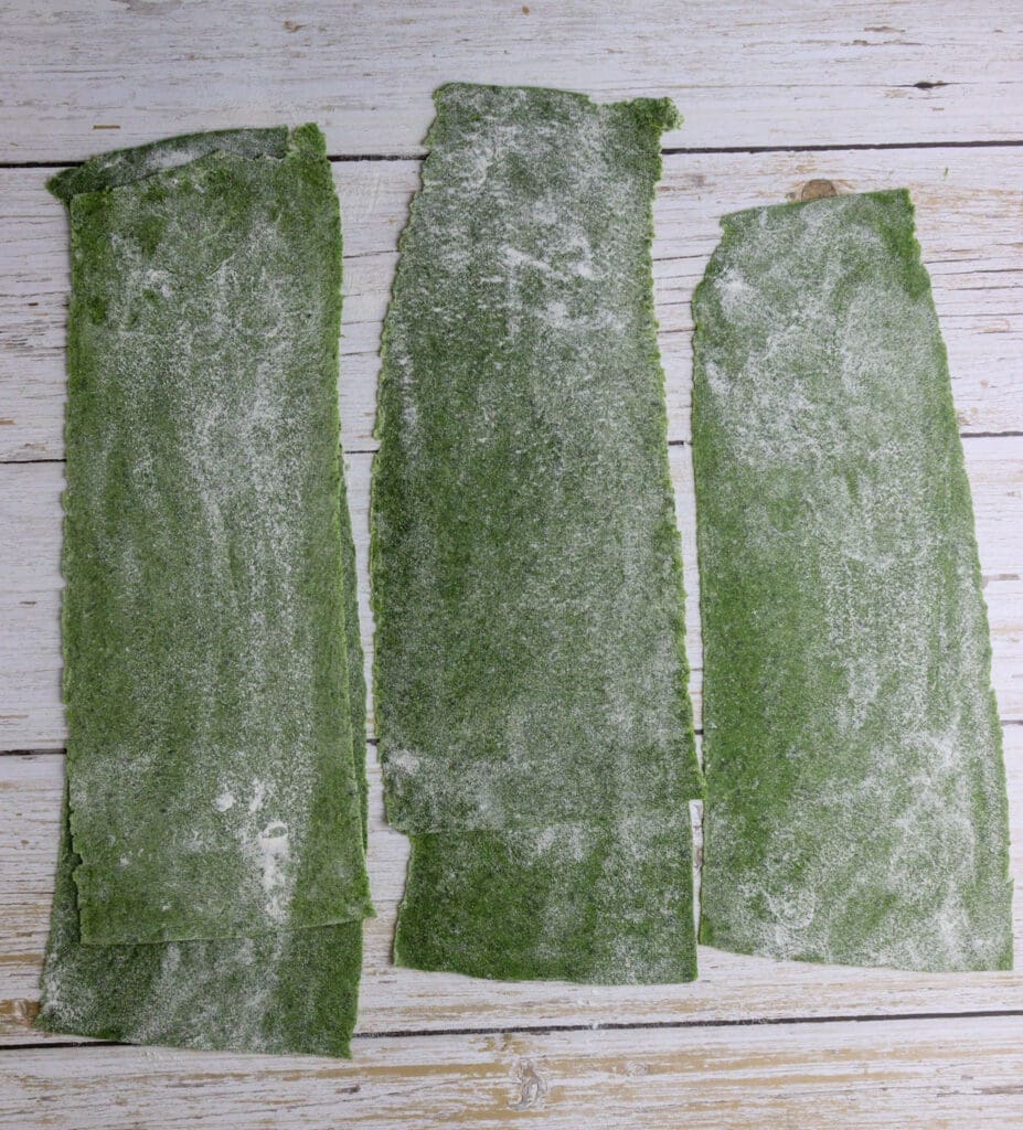 image showing how to sprinkle green wild garlic pasta sheets with flour on both sides to prevent sticking together or sticking to the pasta maker 