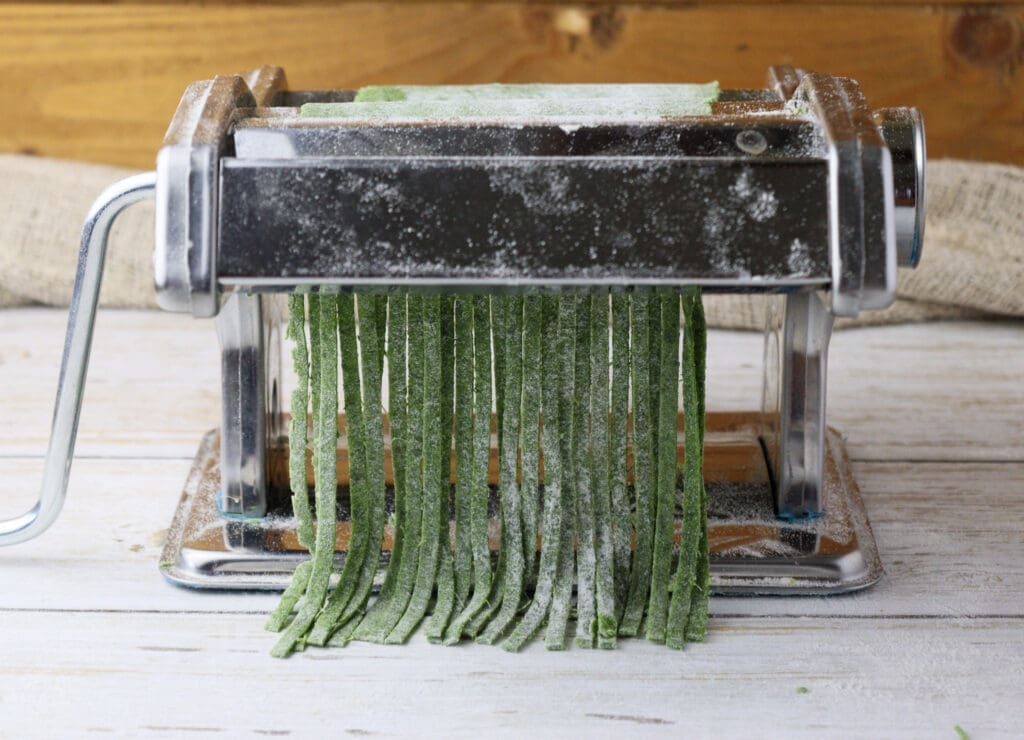 image showing how nice noodles made from green wild garlic pasta dough are coming out of the pasta maker machine 