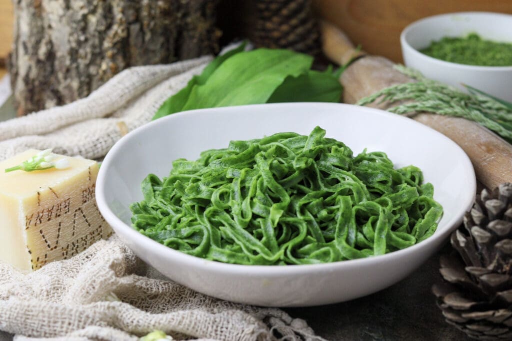 a plate of green wild garlic pasta served with wild garlic pesto and grana padano cheese in the background 