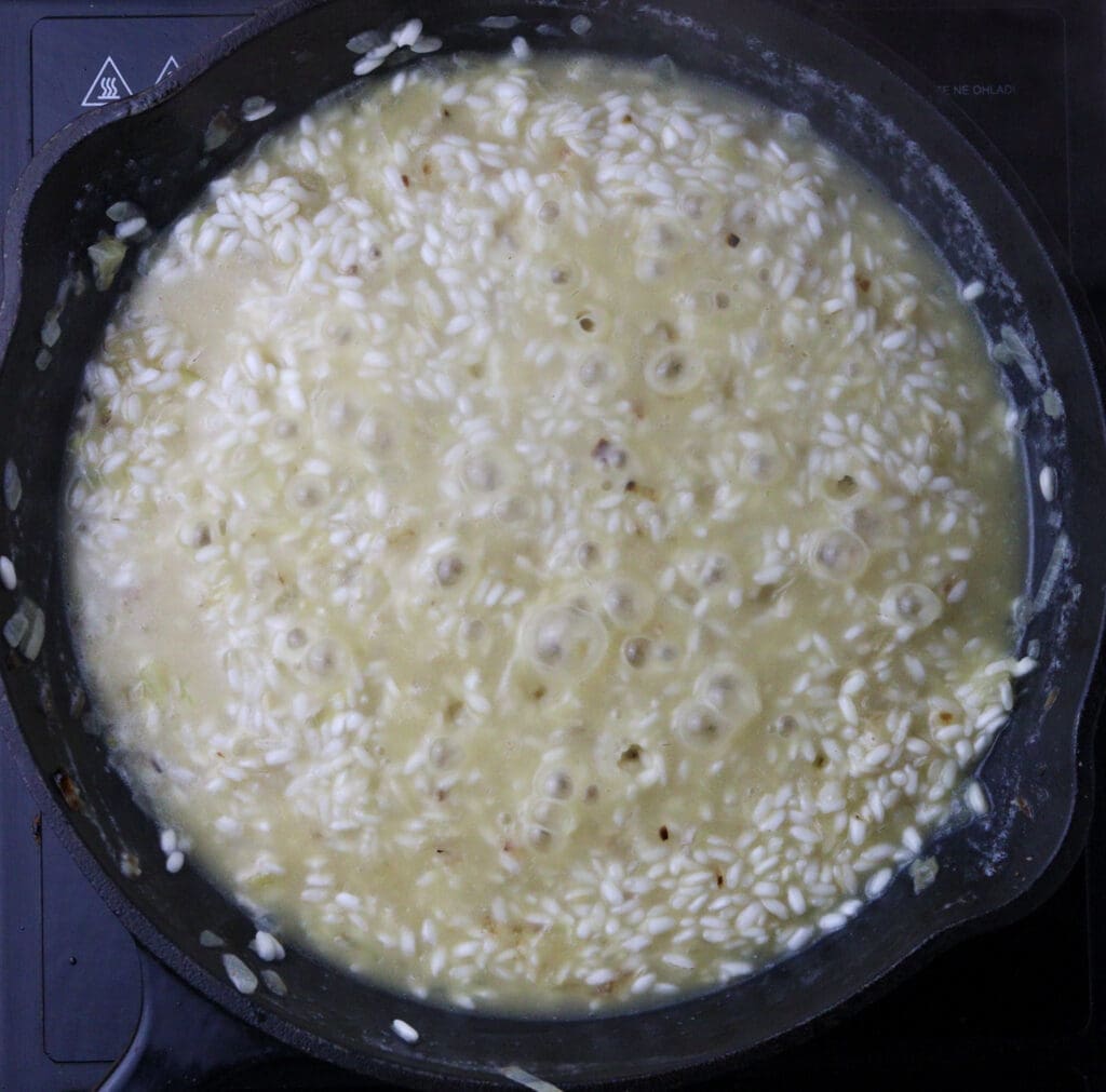 How to keep gradually adding liquid when cooking risotto. Image showig risotto slowly cooking. 