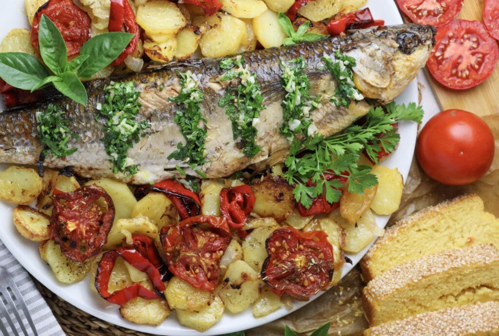 A culinary presentation of grey mullet on a plate, paired with potatoes and tomatoes, exemplifying a delightful recipe.