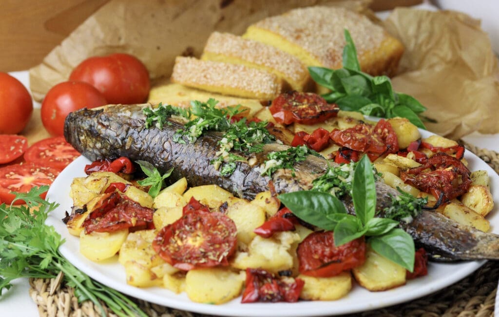 baked grey mullet served on a plate with potatoes, vegetables and garlic-herb sauce