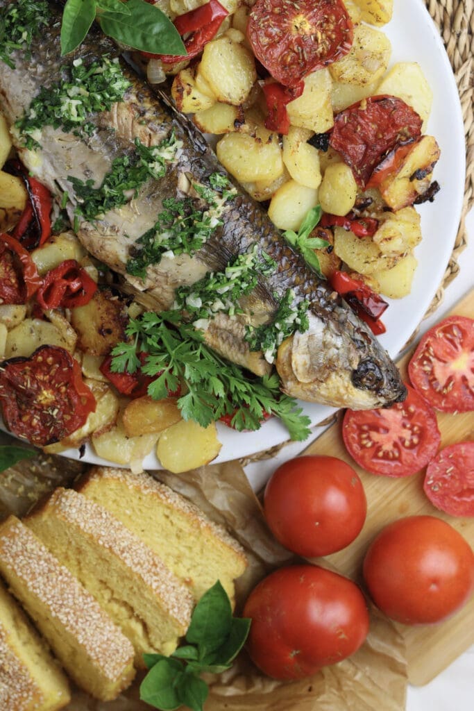 Culinary representation of oven baked grey mullet recipe with roasted vegetables and fresh parsley, tomatoes and corn bread 