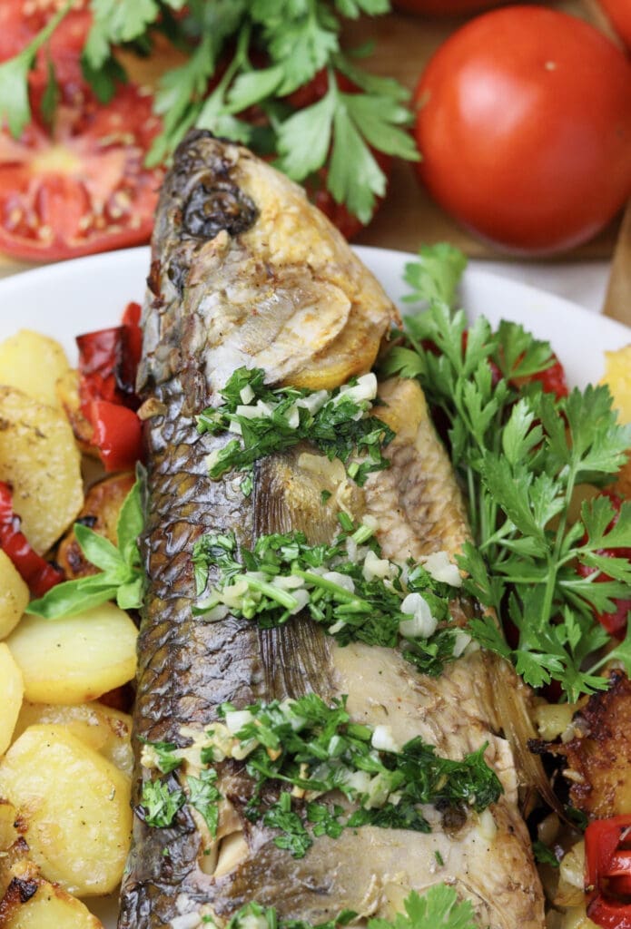 Image showing the head of baked grey mullet topped with garlic sauce and stacked with fresh parsley. 