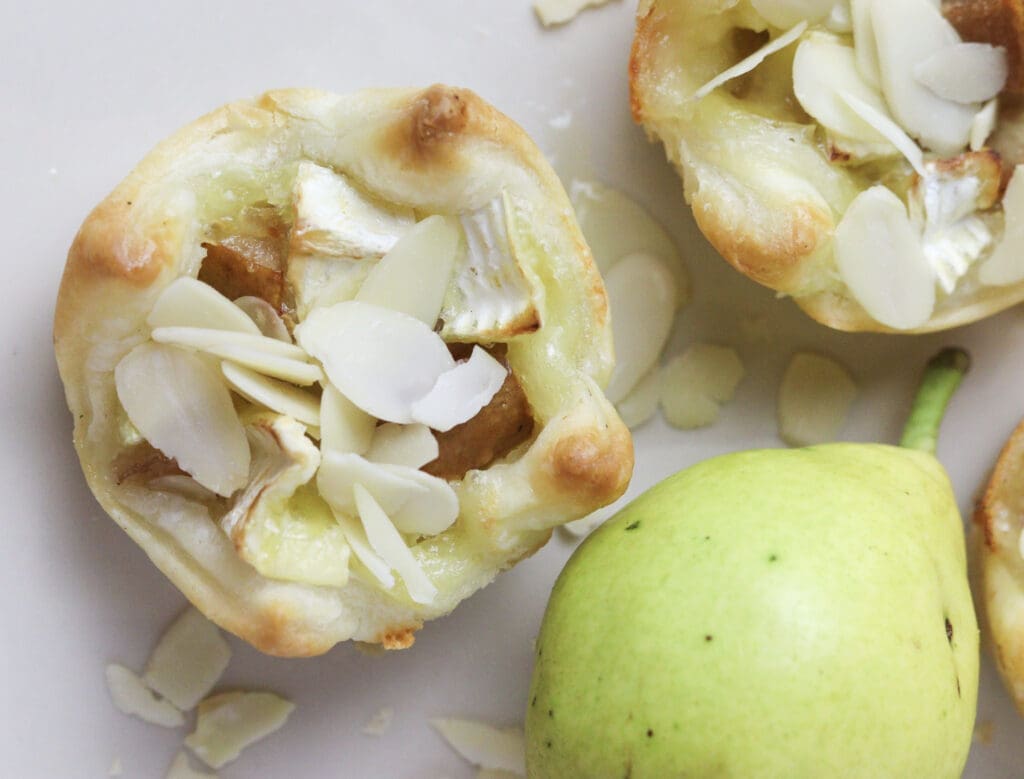 a culinary representation of brie and pear puff pastry bites, sprinkled with honey and almonds on a plate 