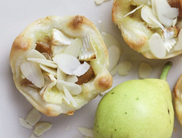 a culinary representation of brie and pear puff pastry bites, sprinkled with honey and almonds on a plate