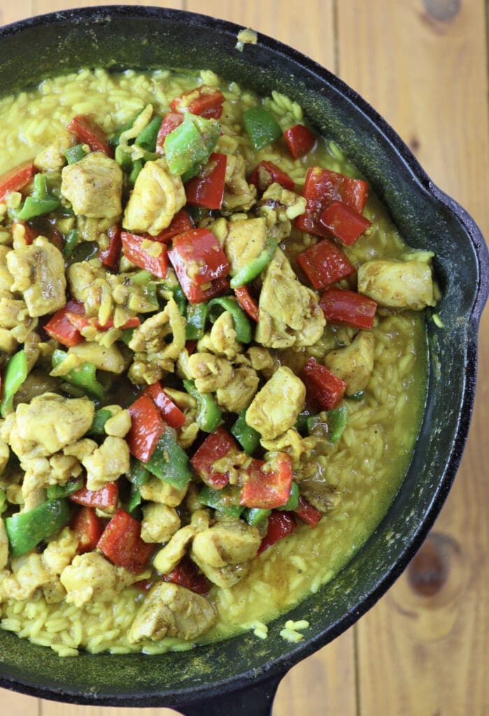 A culinary representation of one pot chicken curry and rice with bell peppers and coconut milk while the dish is still cooking. 