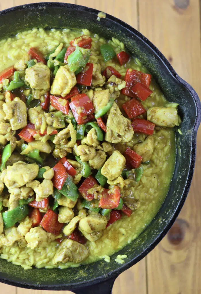 A culinary representation of one pot chicken curry and rice with bell peppers and coconut milk while the dish is still cooking.