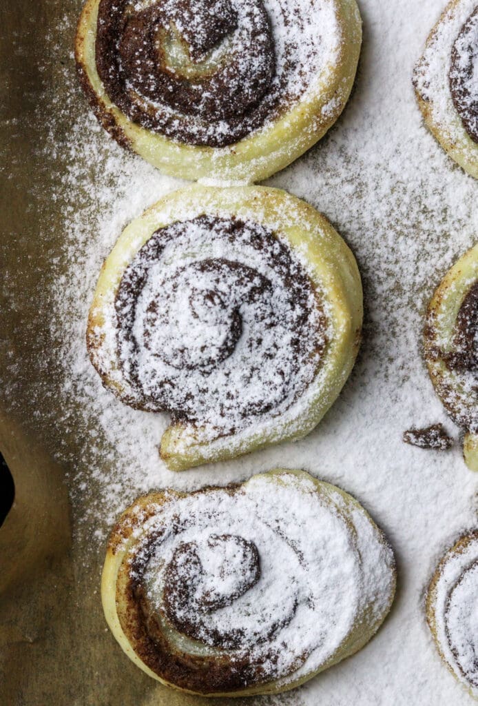 Image of three puff pastry cinnamon pinwheels on a baking tray sprinkled with powdered sugar