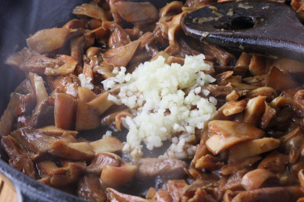 Image of adding crushed garlic to sauted lactarius deliciosus mushrooms