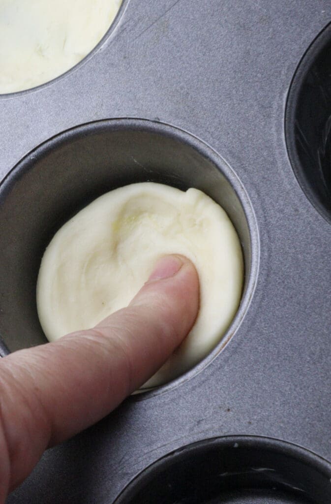 Image showing how to press the puff pastry dough in the muffin tin to form a cup for the filling