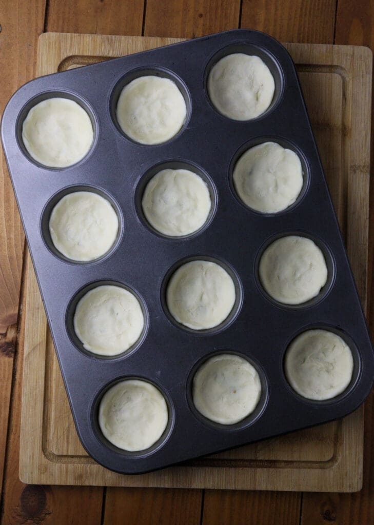 Image showing puff pastry cups in a muffin baking tin before being filled with saffron milk cap cheese mixture. 