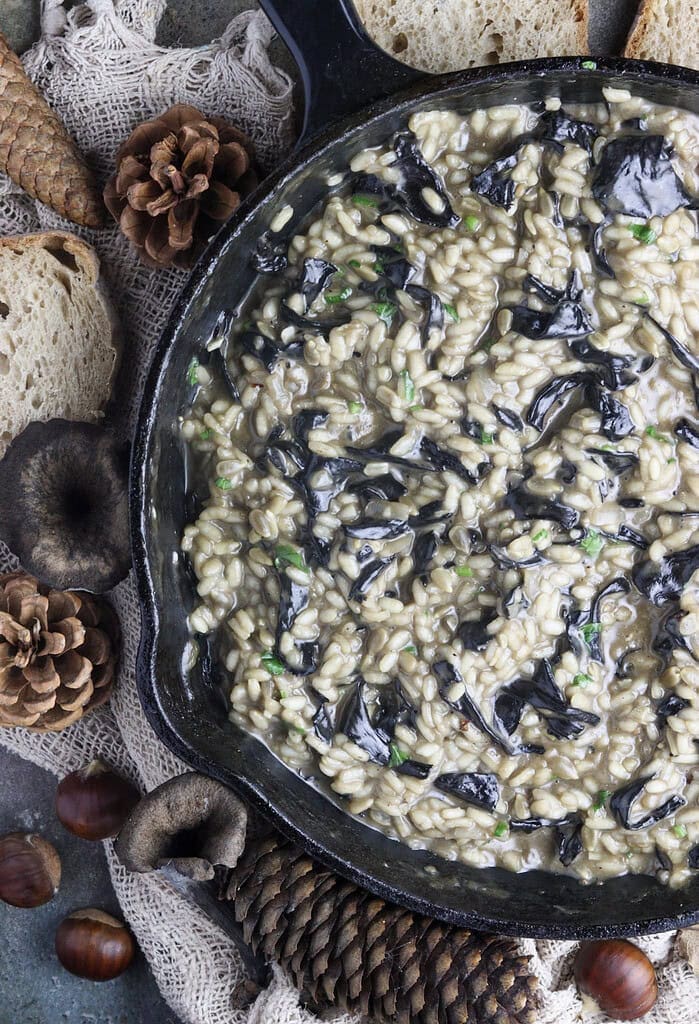 image of a pan, full of black trumpet risotto with served bread and decoration