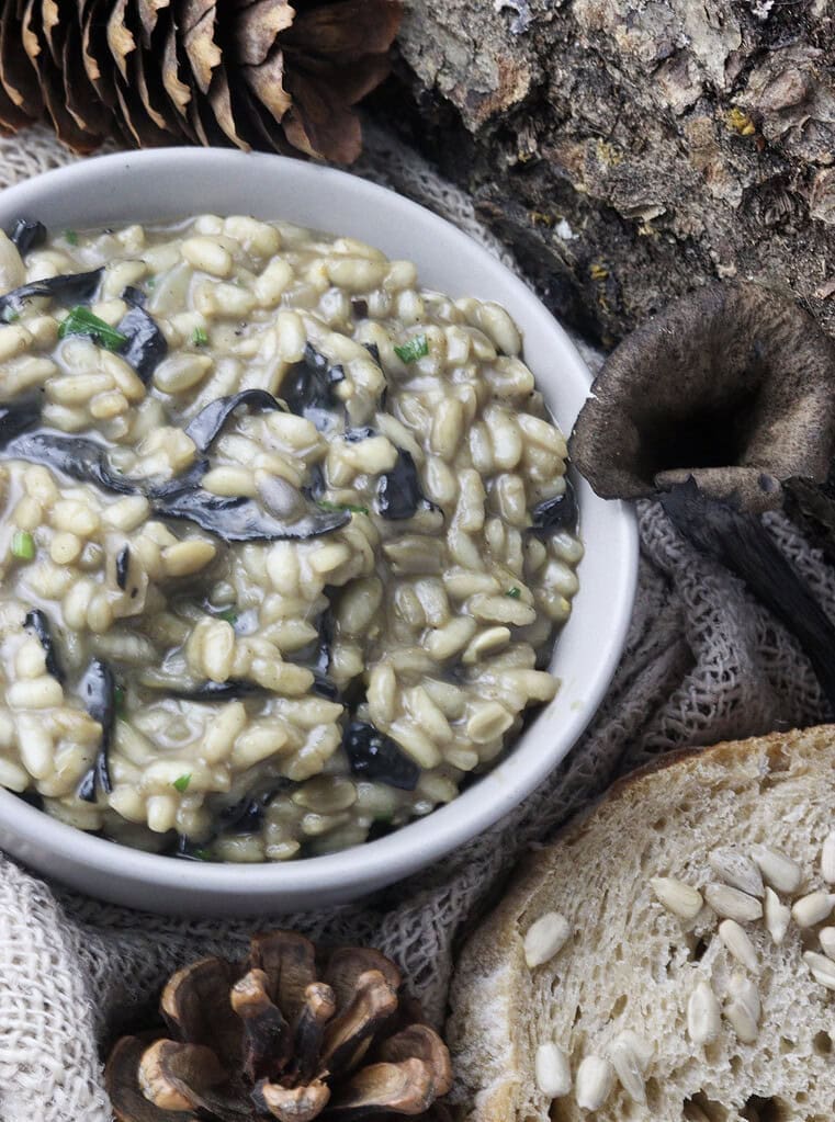 a bowl of black trumpet risotto with bread amd black trumpet mushroom beside it