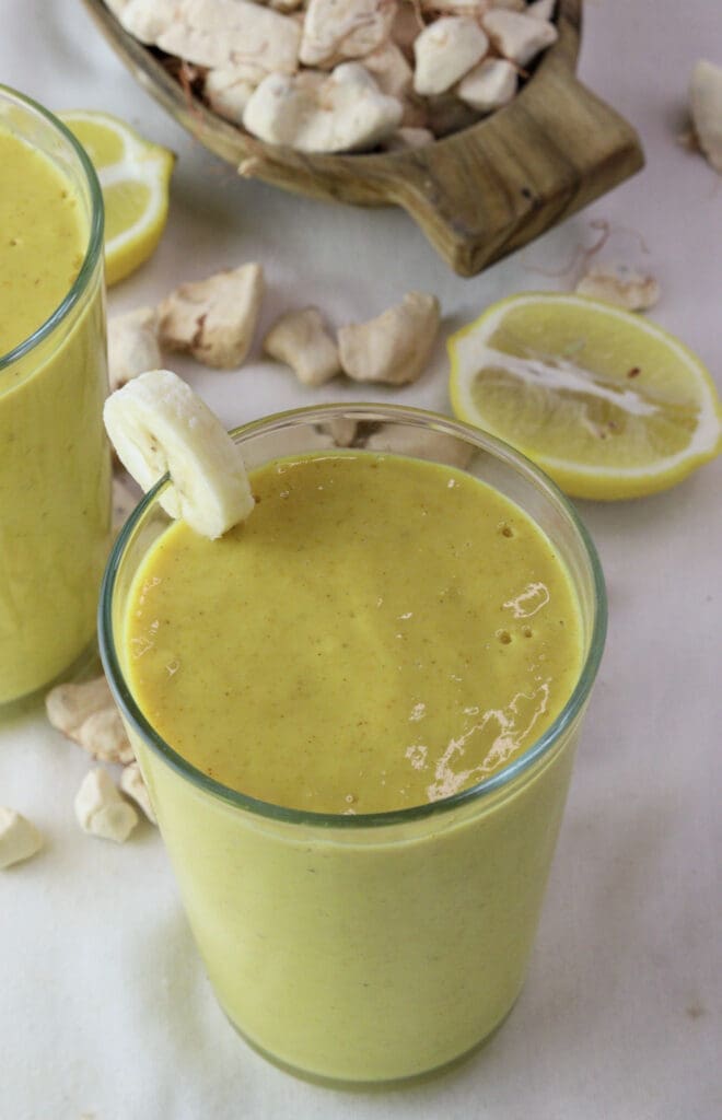 Image of a glass full of baobab smoothie with ginger with baobab fruit and lemons in the background. 