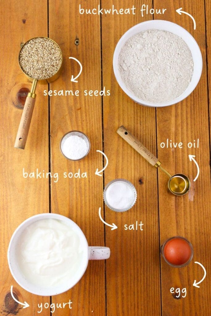 Image of ingredients needed for gluten-free buckwheat soda bread: buckwheat flour, yogurt, sesame seeds, olive oil, salt, baking soda, one egg.