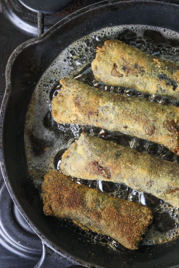 Mushroom rolls frying in hot oil, becoming golden and crispy.