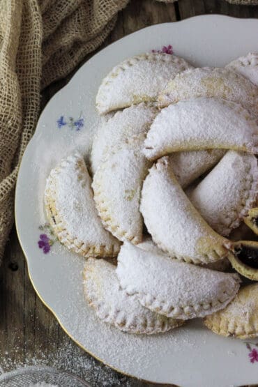 A stack of wonderully tasty empanada cookies stacked on a rustic, old fashioned plate