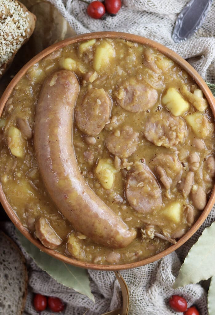 Top view of a portion of Slovenian jota soup with a big half of carniolan sausage served on top.