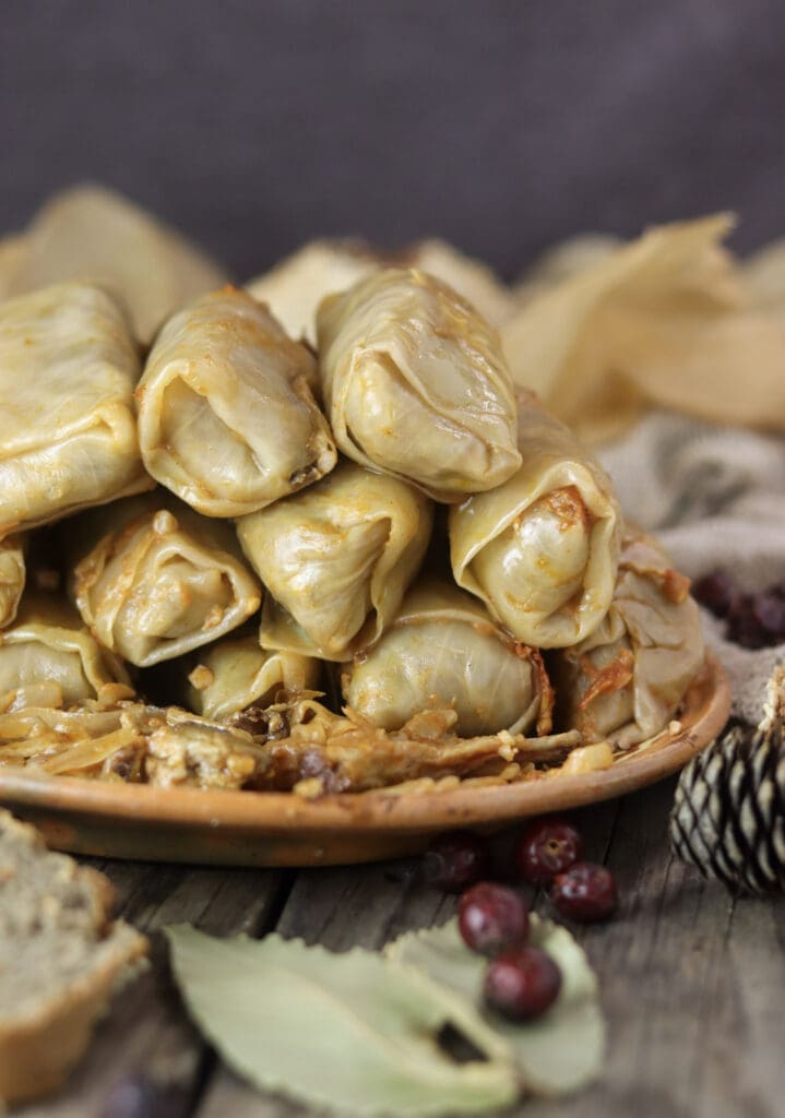 A plate full of baked stuffed cabbage rolls with buckwheat with bay leaves and homemade bread in front of the plate.