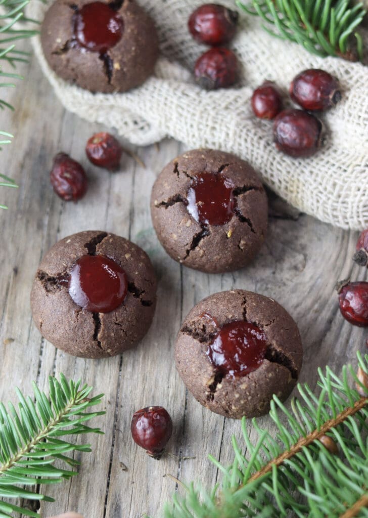 Three buckwheat cookies on a wooden table with silver fir and rosehip buds in the background