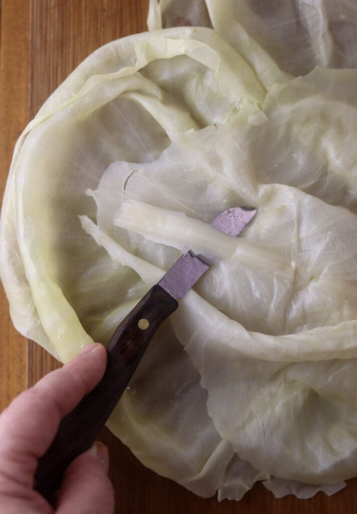 Using a knife to thin the stem of a sour cabbage leaf before making stuffed cabbage rolls.