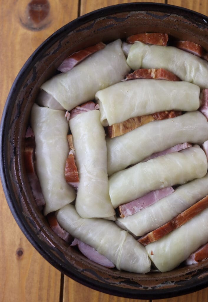 Adding cabbage rolls to the baking pot and stuffing slices of smoked pork ribs in between the rolls.