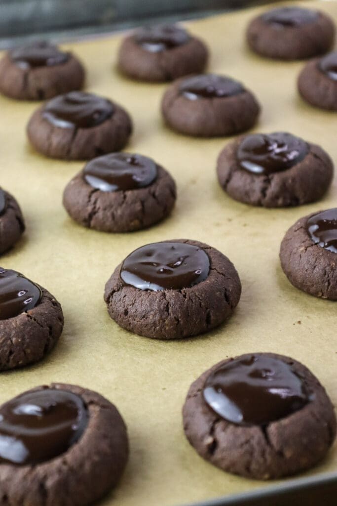 Buckwheat chocolate thumprint cookies on a baking sheet, freshly filled with hot chocolate filling.
