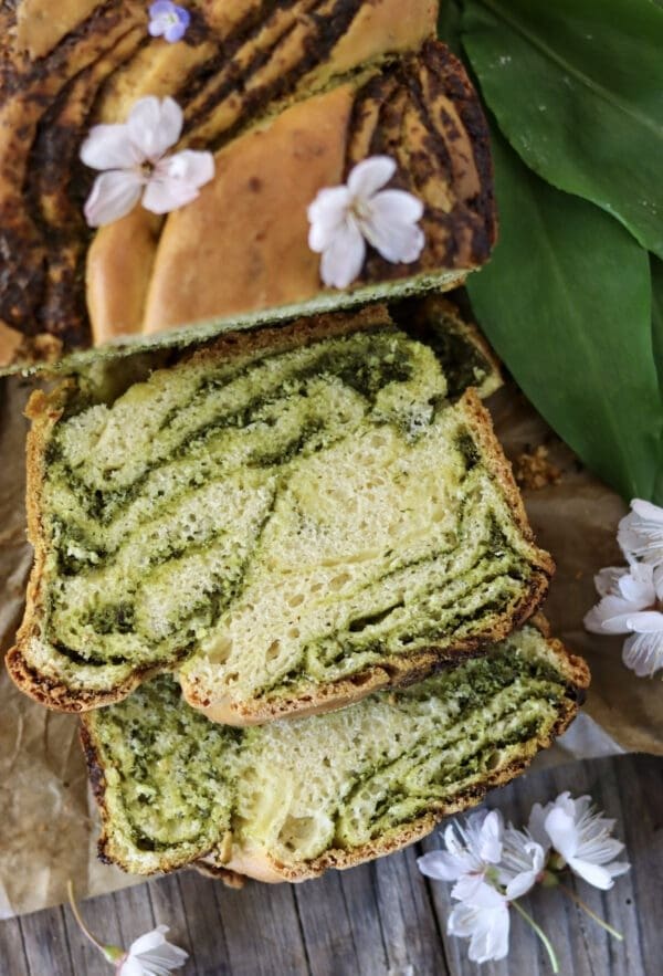 Slices of wild garlic bread with wild garlic leaves and cherry flowers in the background.